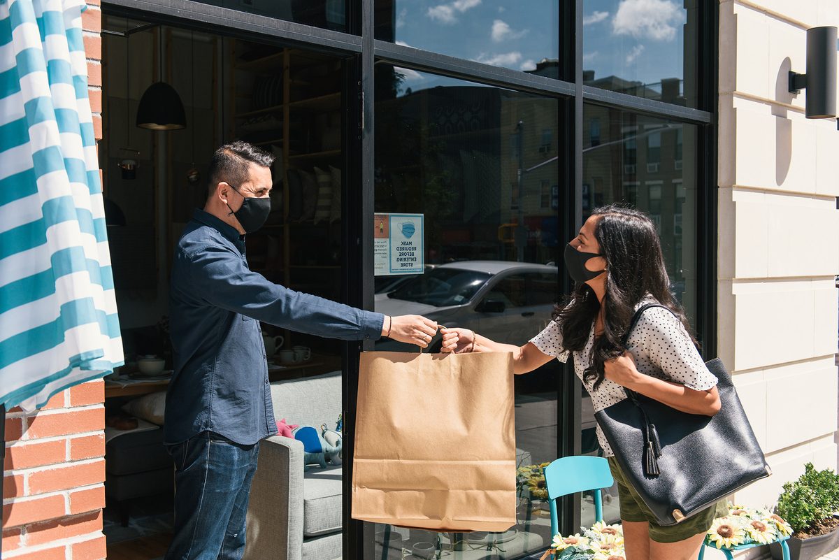 Store employee wearing a mask handing customer a paper bag