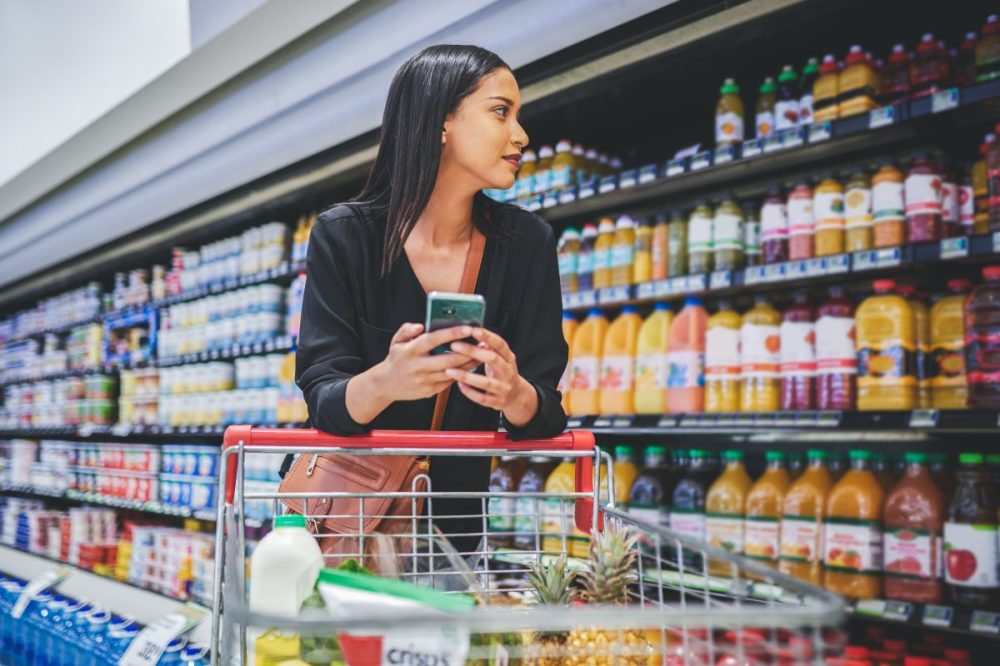 A young woman USES a smartphone while shopping in a grocery store