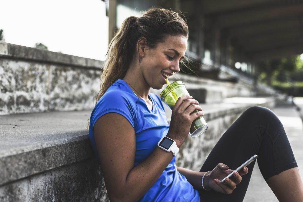 Young woman sitting on step with cell phone and drinking cup