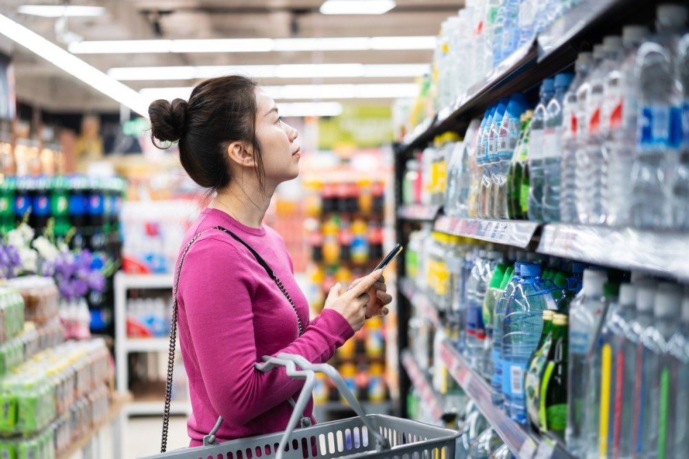 asian female using smart phone while shopping in supermarket