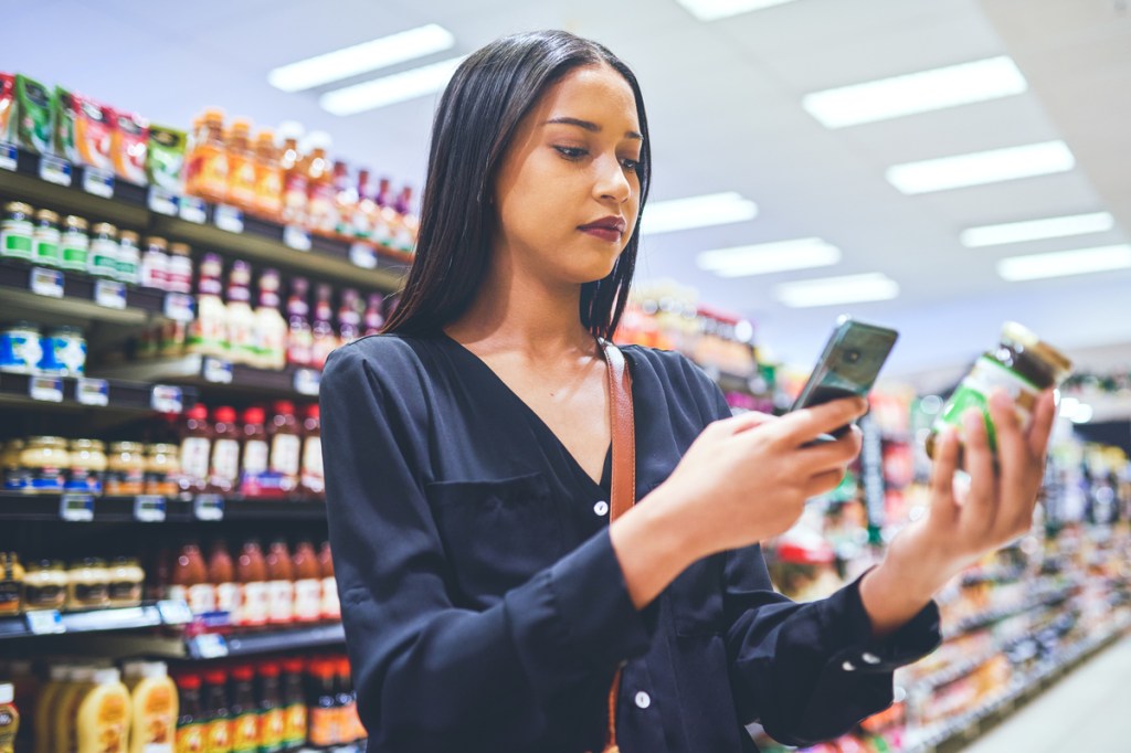 Shot of a young woman using a smartphone while shopping in a grocery store