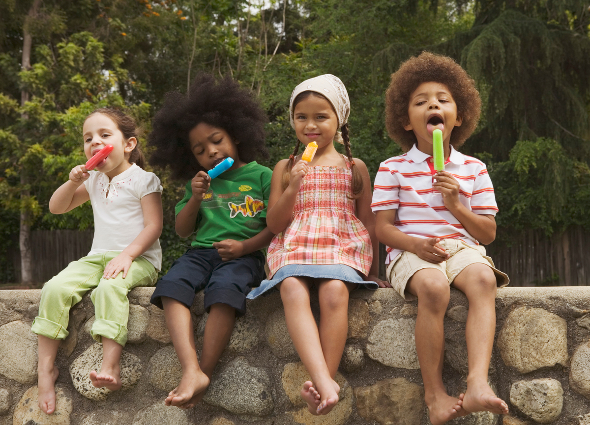 Four children sitting on a stone ledge eating popsicles