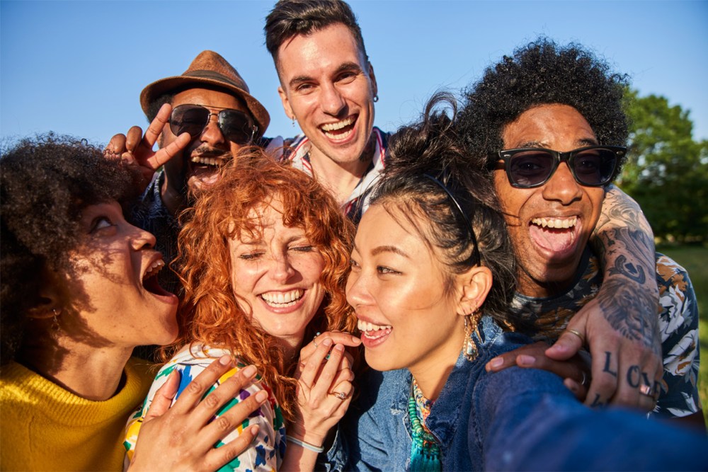 A group of 6 multicultural Gen Z members, hugging each other and smiling while standing outside.