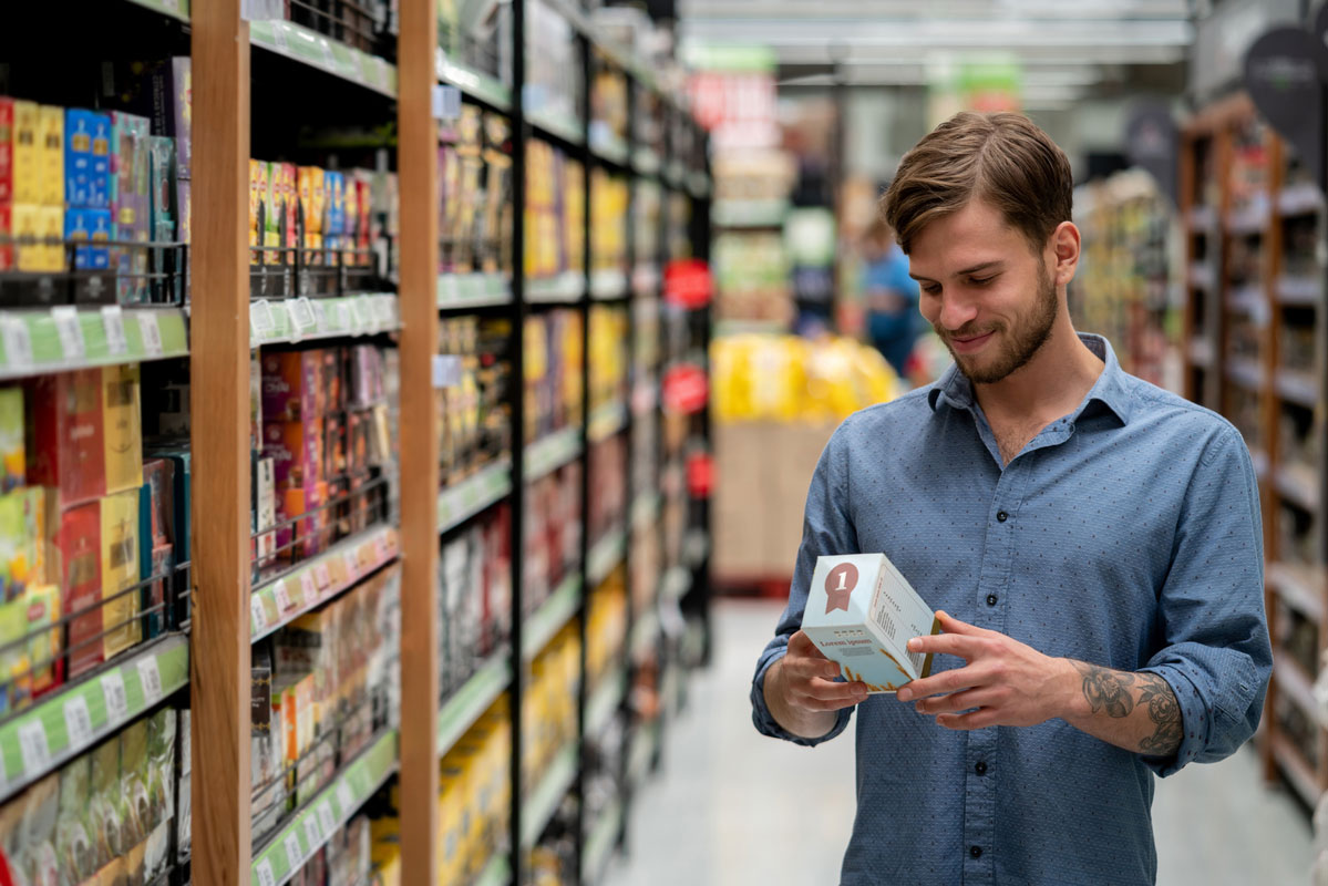 Man with blue shirt holding product looking at the label in a store aisle