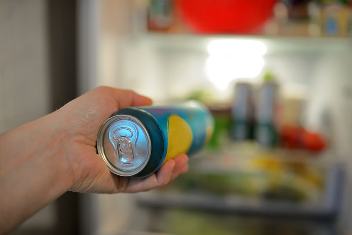 Hand holding beverage can in front of open refrigerator