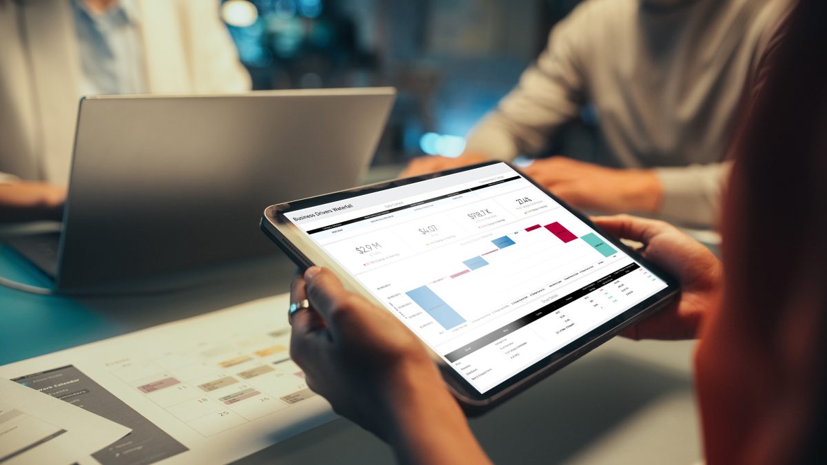 Woman holds a tablet that has charts and graphs on the screen in a meeting with 2 others