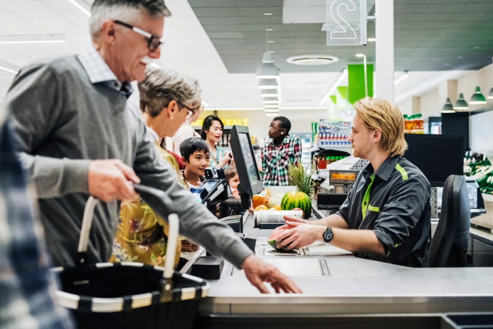 A cashier ringing up a senior couple's groceries so they can pay at their local supermarket.