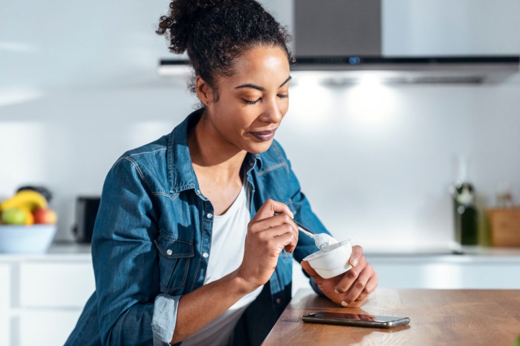 Women in Jean jacket eating yogurt in her kitchen