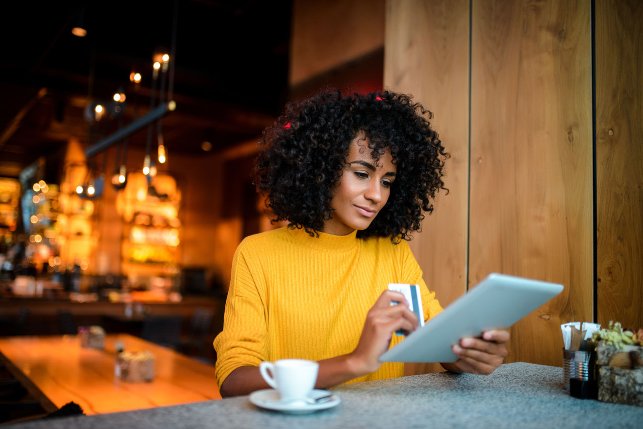 Woman with dark curly hair and a yellow shirt making a purchase with a credit card on her tablet