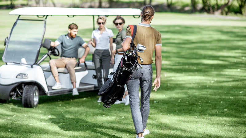 Golfer with golf bag over his shoulder heading toward a golf cart with 3 other golfers