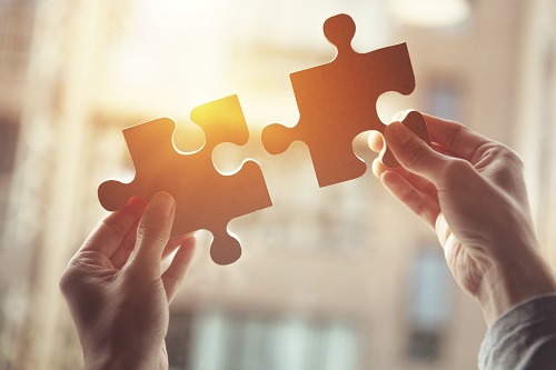 Person holding two large puzzle pieces together in a sun lit room