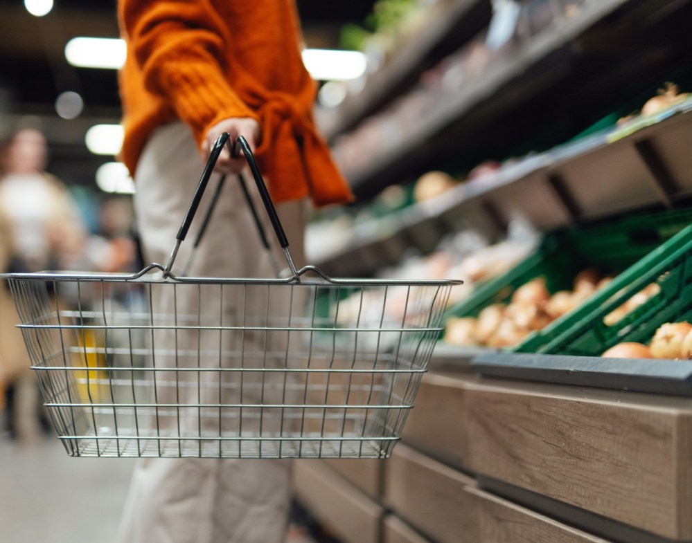 Lower section of young woman standing next to product aisle and choosing vegetables in the store. Young Asian woman doing grocery shopping in supermarket.