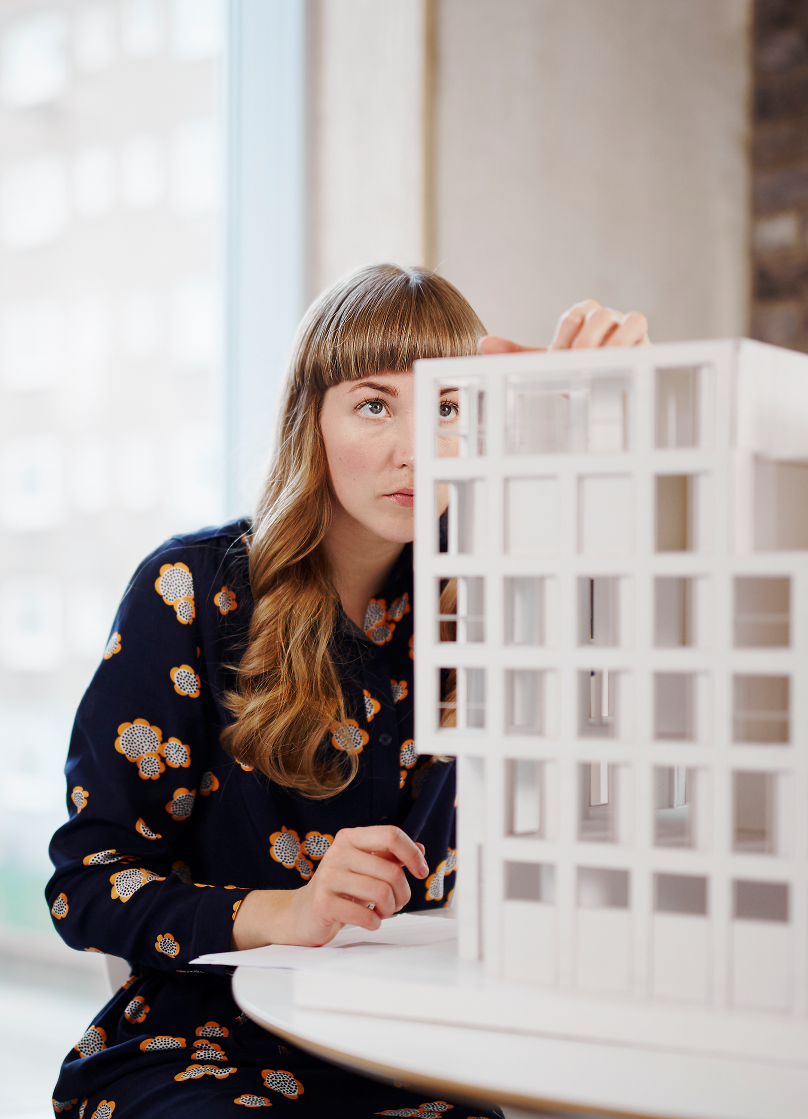 Woman with coloful blouse and long blond hair looking at a model of a building