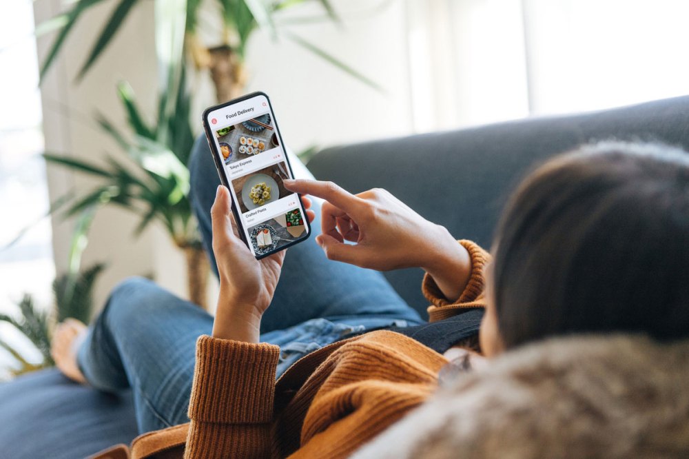 Woman with orange sweater and jeans lying on a couch using her phone