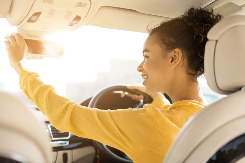A young girl in a yellow shirt adjust the rearview mirror in a car